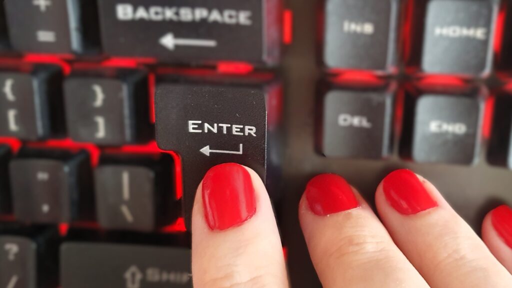 red nails on mechanical keyboard with red backlight pressing the enter key
